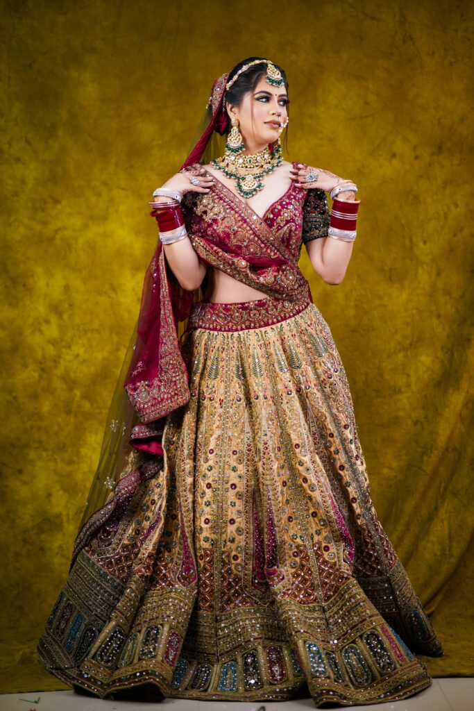 Bride wearing a traditional maroon and mustard designer bridal lehenga with heavy embroidery, jewellery, and red bangles — perfect representation of lehenga for women at Indian weddings.